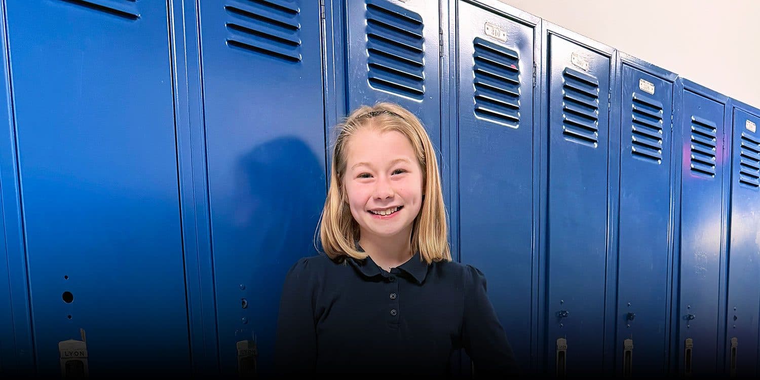 Smiling student standing in front of lockers in a school hallway.