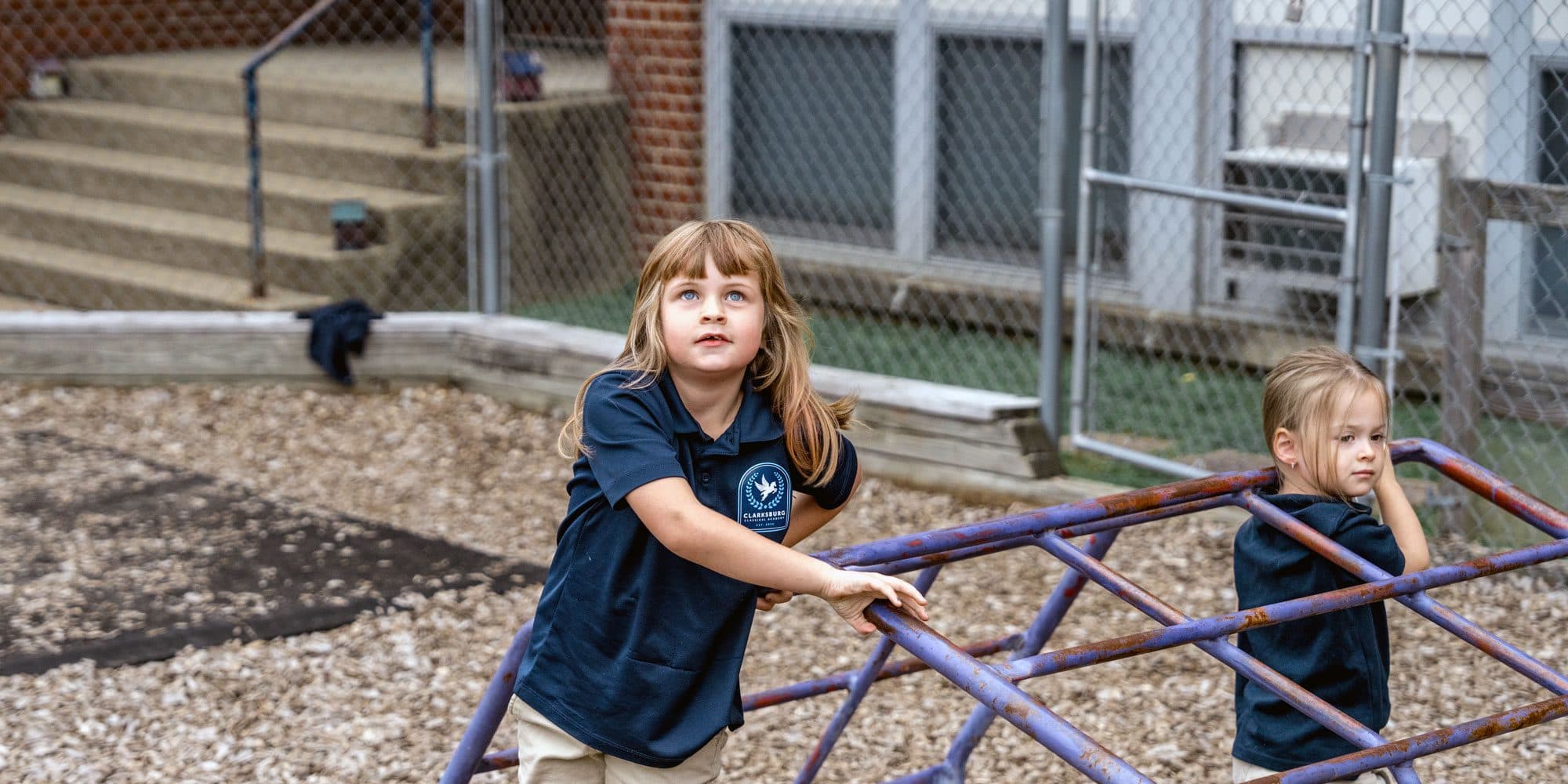 Two students in school uniforms at a climbing structure on the playground.