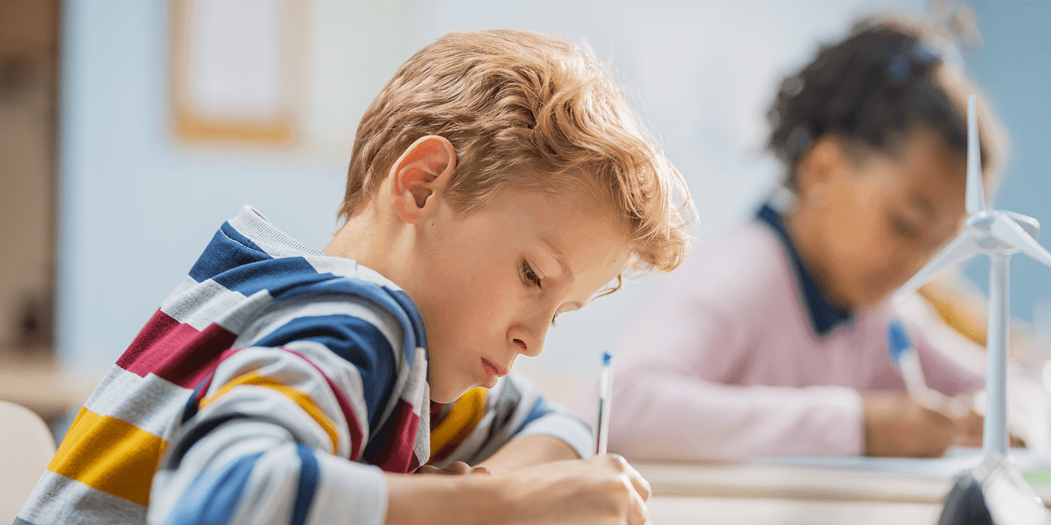 Child writing at a desk with a pen, focused on their work.