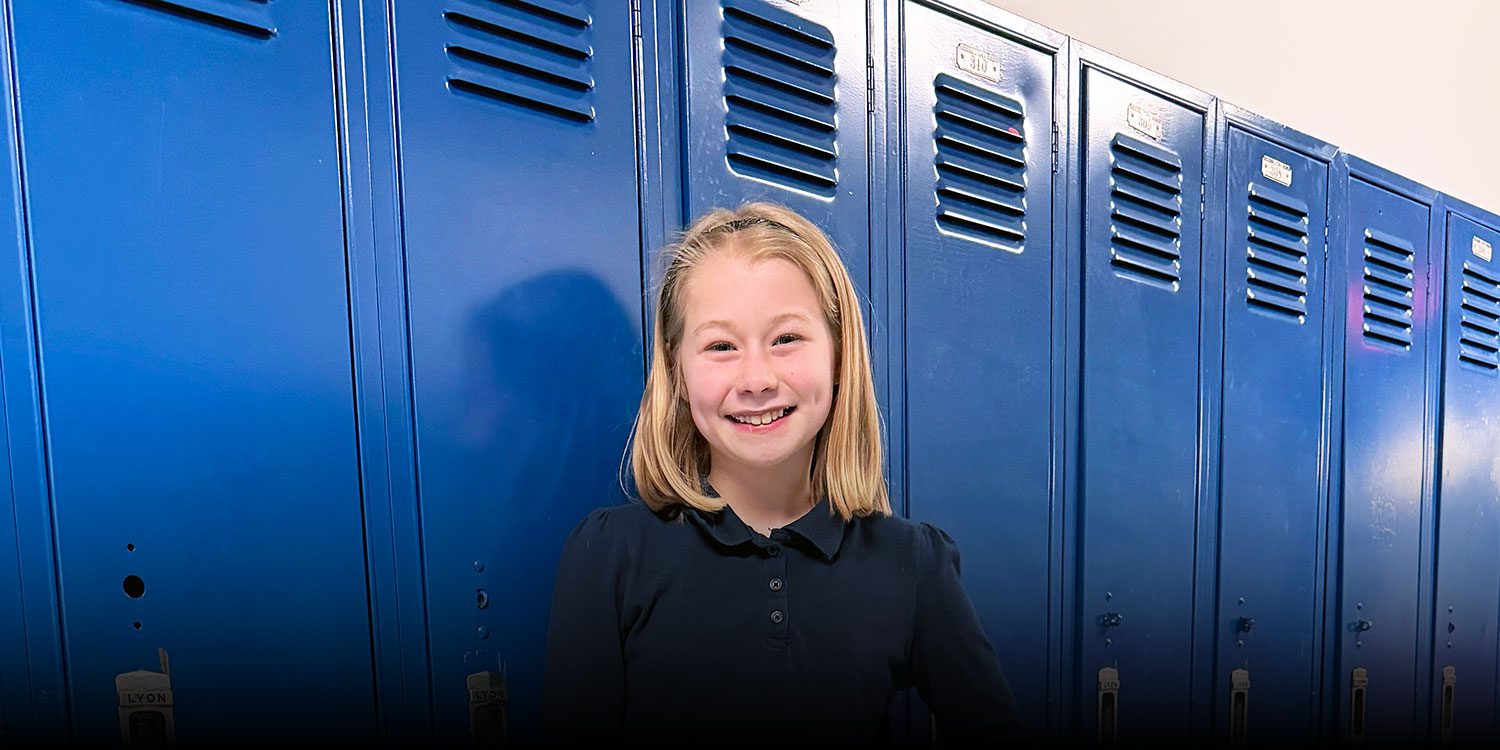 Smiling student standing in front of lockers in a school hallway.